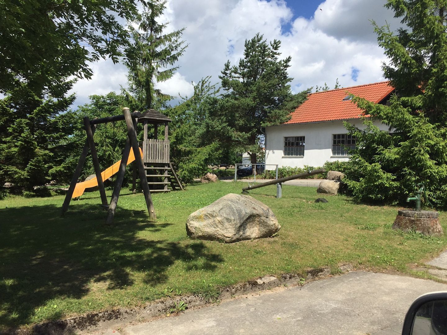 Ein Spielplatz mit Rutsche und Klettergerüst, einem großen Felsen und einem Haus mit rotem Dach.