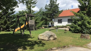 Ein Spielplatz mit Rutsche und Klettergerüst, einem großen Felsen und einem Haus mit rotem Dach.