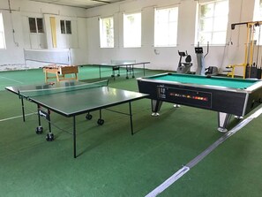 Une salle de billard équipée de deux tables de billard, d’une table de baby-foot et d’une table de ping-pong.