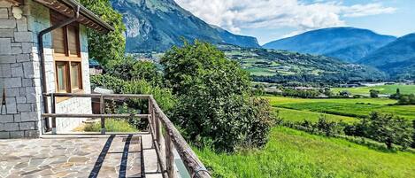 A stone building with a balcony overlooking a green valley and mountains.