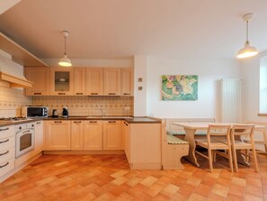 A kitchen with wooden cabinets, a dining table with chairs, a microwave, a stove, and a sink.