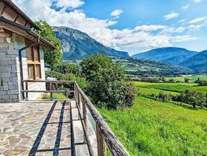 Un edificio in pietra con un balcone che si affaccia su una valle verde e montagne.