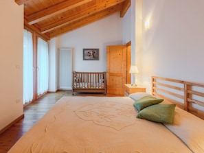 Een slaapkamer met een houten plafond, een bed met bloemenbedekking, een nachtkastje met een lamp, een houten garderobe en een raam met gordijnen.