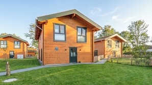 A two-story wooden house with a green door, a small front porch, and a well-maintained lawn.