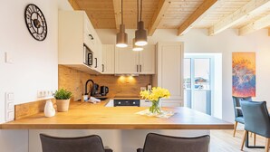 A modern kitchen with wooden countertops, a central island with chairs, pendant lighting, and a large window.