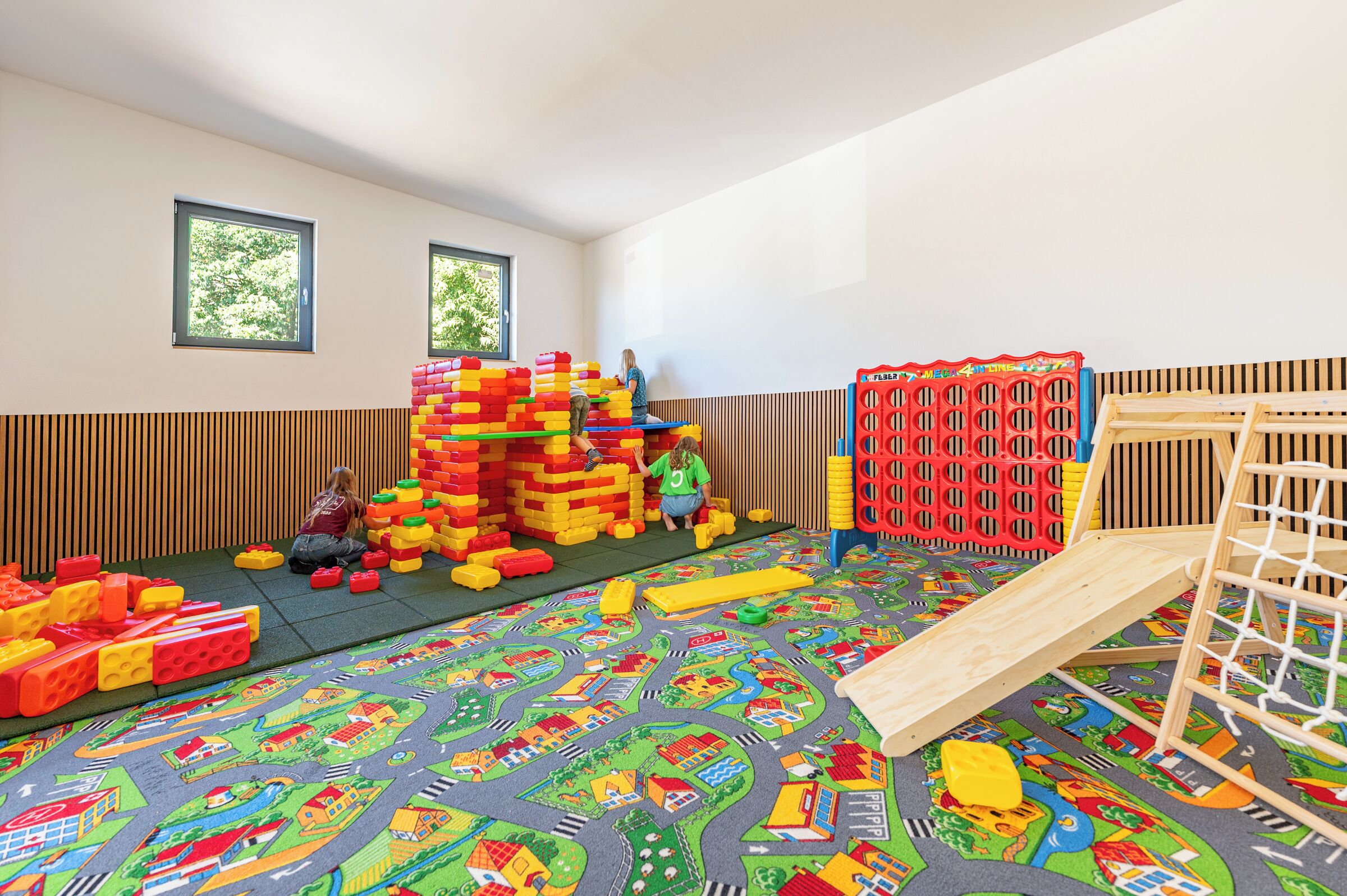 A playroom with a soft play mat, a wooden play structure, and a large stack of colorful building blocks.