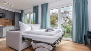 A modern bedroom with a pull-out bed, a kitchen area, and large windows with curtains. - Vacation apartments near the beach on the pier (Graal-Müritz)