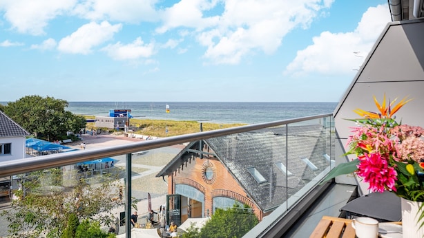 A balcony with a view of the beach and sea, a flower arrangement, and a table with a cup. - Vacation apartments near the beach on the pier (Graal-Müritz)