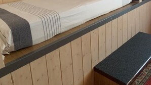 A single bed with a grey and white striped blanket, a wooden desk with a lamp, and a bench. - Magnificent apartment overlooking the Vallée Verte (Habère-Lullin)