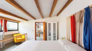 Ein Schlafzimmer mit einem Bett, einem Schreibtisch und einem Sessel. Eine Tür führt in einen anderen Raum.