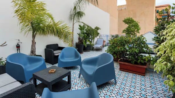 Eine Dachterrasse mit Außenmöbeln, Pflanzgefäßen und einem gemusterten Boden.