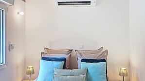 A bedroom with a bed, two bedside tables with lamps, an air conditioning unit on the wall, and a window.