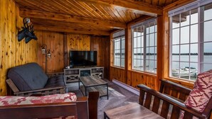 A cozy cabin interior with wooden walls, a television, seating area, and a view of the water. - Multi-unit with lake access (Fife Lake)