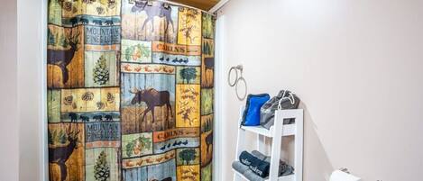 A bathroom with a wooden ceiling, a shower curtain with wildlife and cabin-themed designs, a towel rack with towels, and a toilet paper holder.