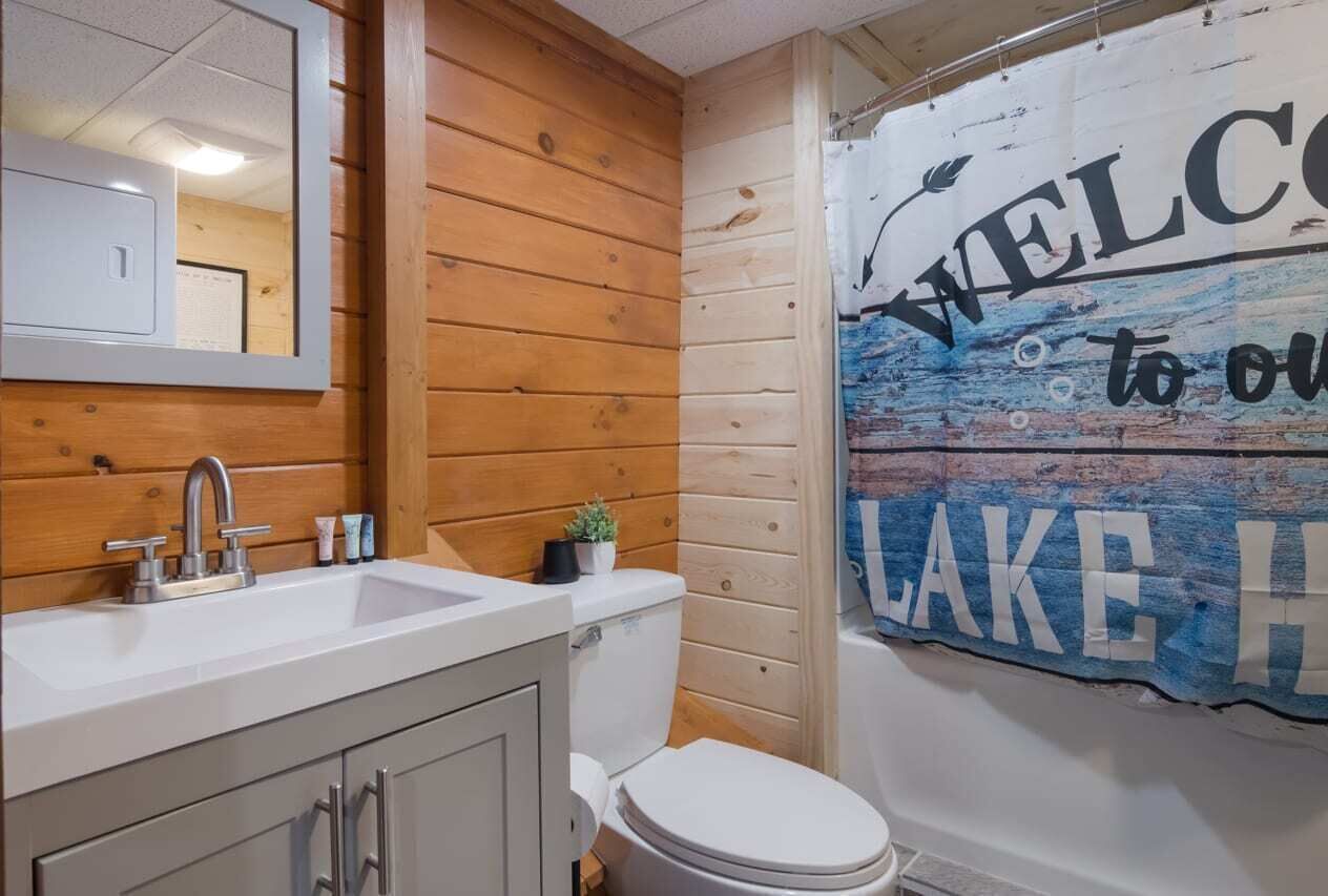 Et badeværelse med trævægge, en hvid vask og et toilet. Velkomstskilt til søen.