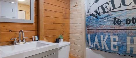 A bathroom with wooden walls, a white sink, and a toilet. There is a welcome sign to the lake.