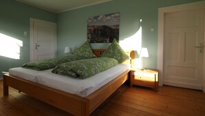 A bedroom with a wooden bed, green floral bedding, a nightstand with a lamp, and a door.