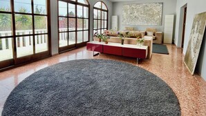 Amplia sala de estar con ventanas arqueadas, un sofá moderno, una consola roja y un ventilador de techo.