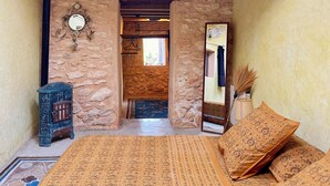 Un dormitorio con pared de piedra, cama con ropa de cama estampada, un pequeño armario de madera y un espejo.