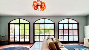 Un salón amplio con un sofá modular grande, una lámpara decorativa y tres ventanas arqueadas que dan al exterior.