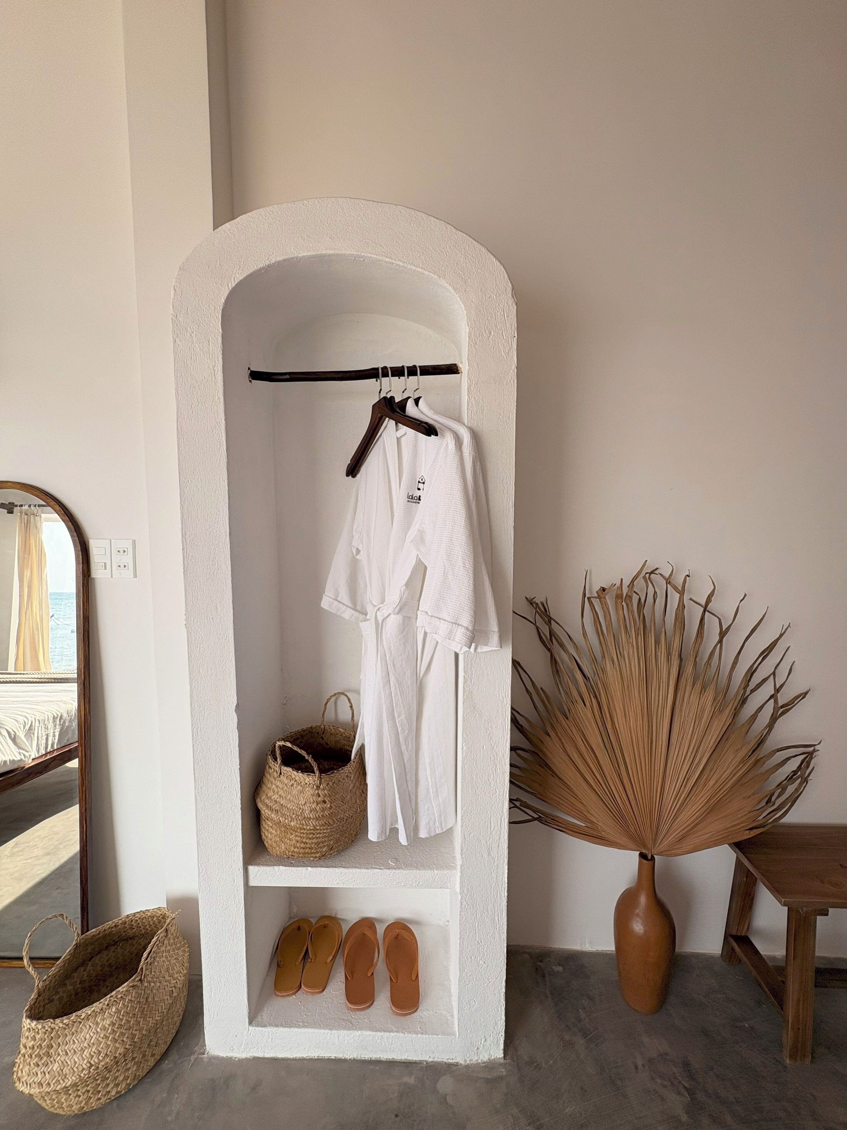 Une étagère blanche en forme d’arc, sur laquelle sont posés un peignoir, un panier tressé et une paire de chaussons.
