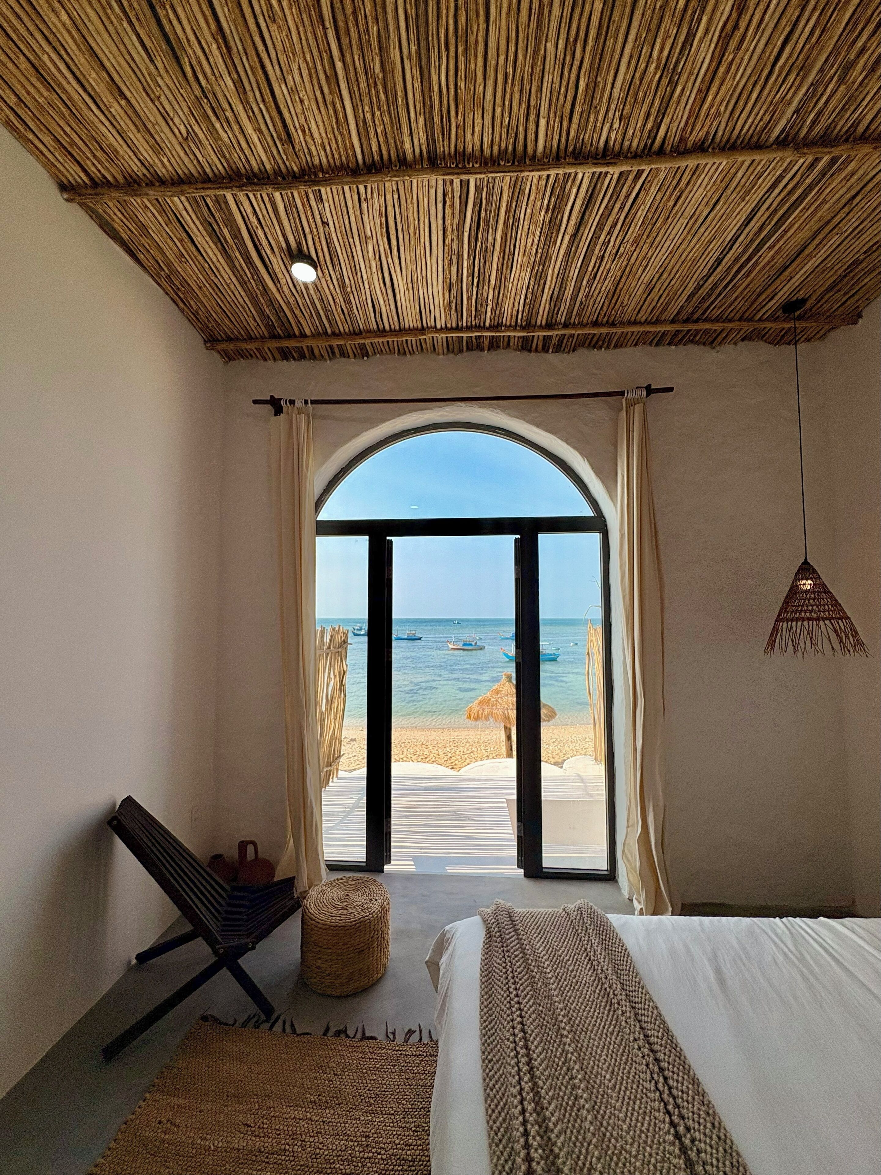 A bedroom with a large window, a bed, a chair, and a hanging light fixture.