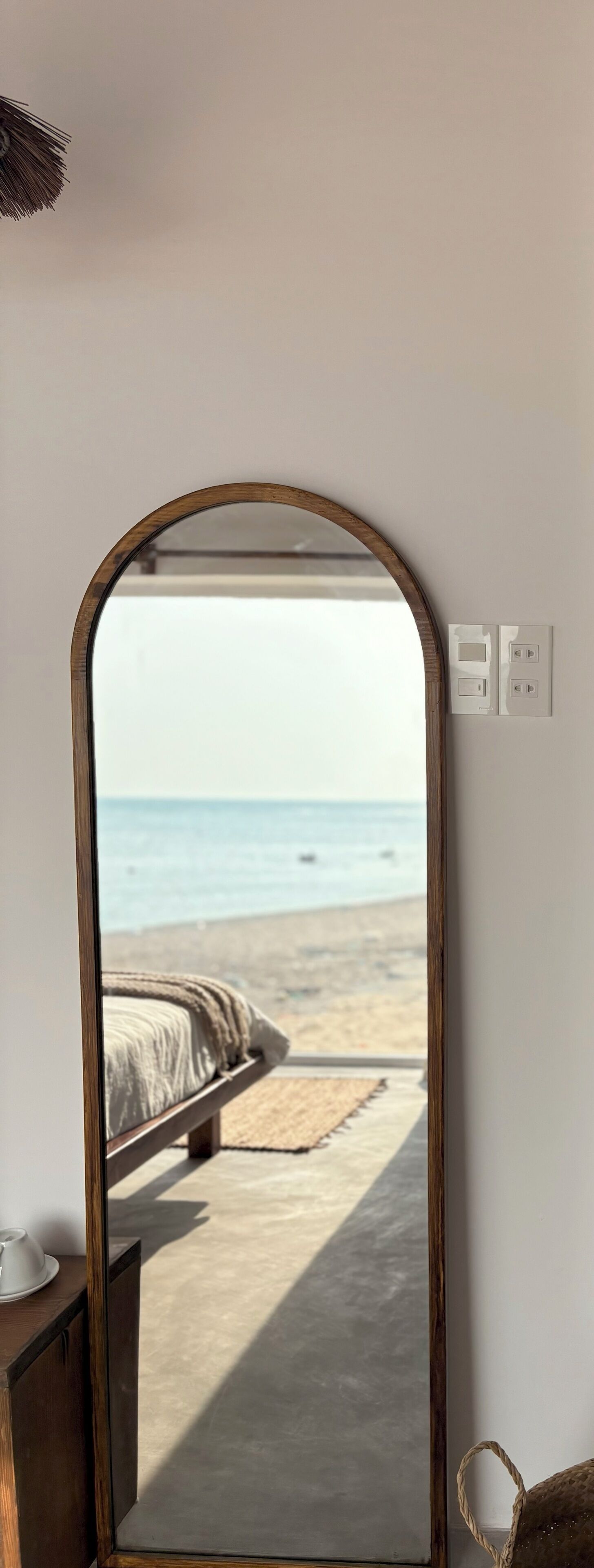 Ein Spiegelbild zeigt ein Schlafzimmer mit Bett, Nachttisch und Blick auf den Strand.