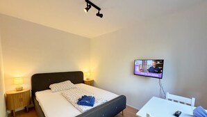 A hotel room with a bed, bedside lamps, a TV on the wall, and a small table with a chair. - Landpension Dubnitz, double room 5 (Sassnitz)