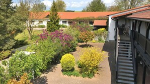 A garden with various plants and a building with a red roof. - Landpension Dubnitz, double room 5 (Sassnitz)