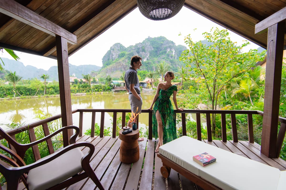 A wooden deck with a bench and a table, overlooking a calm river and lush greenery.