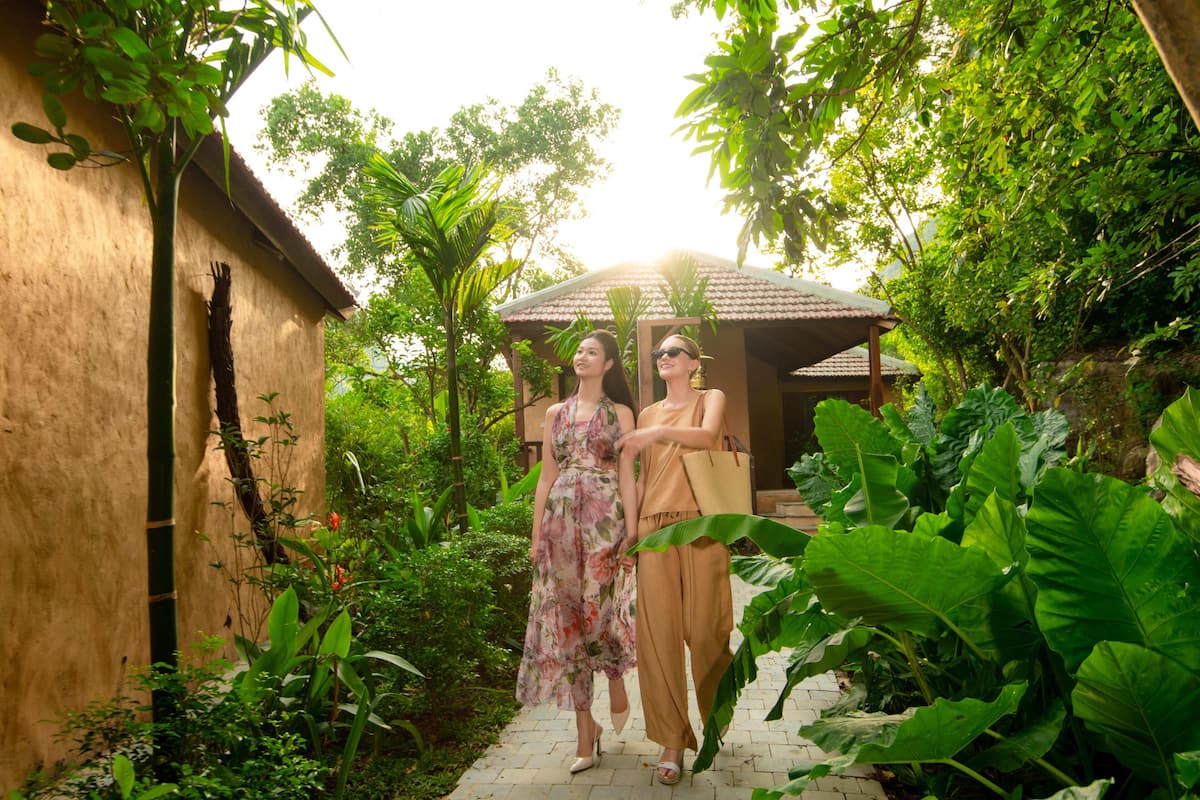 A pathway leading to a building with a tiled roof, surrounded by lush greenery and large plants.