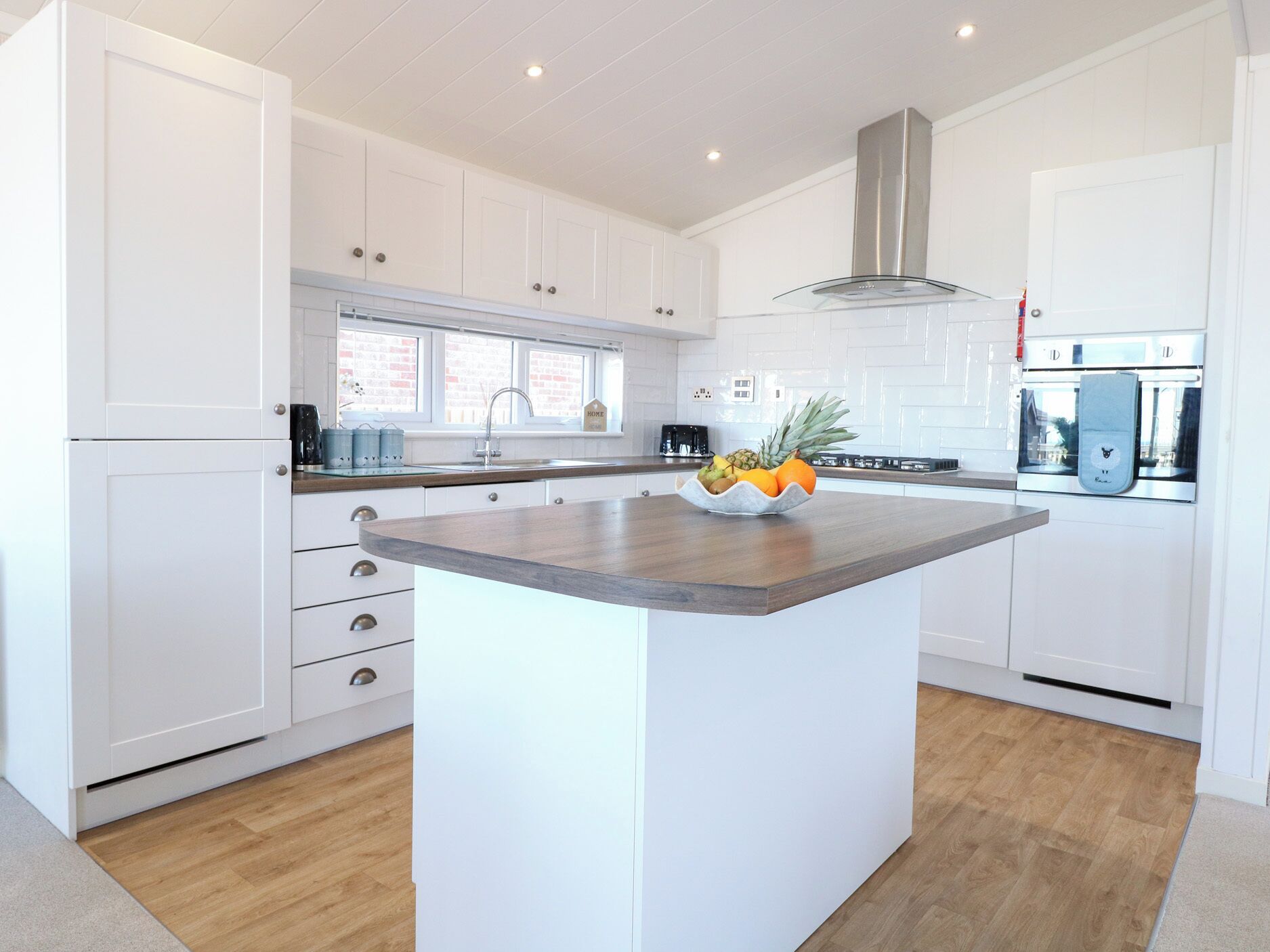A modern kitchen with white cabinetry, a central island, and a stainless steel range hood.