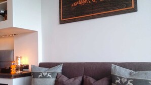 A living room with a dark-colored sofa, two grey pillows with deer and heart patterns, and a framed picture of mountains on the wall.