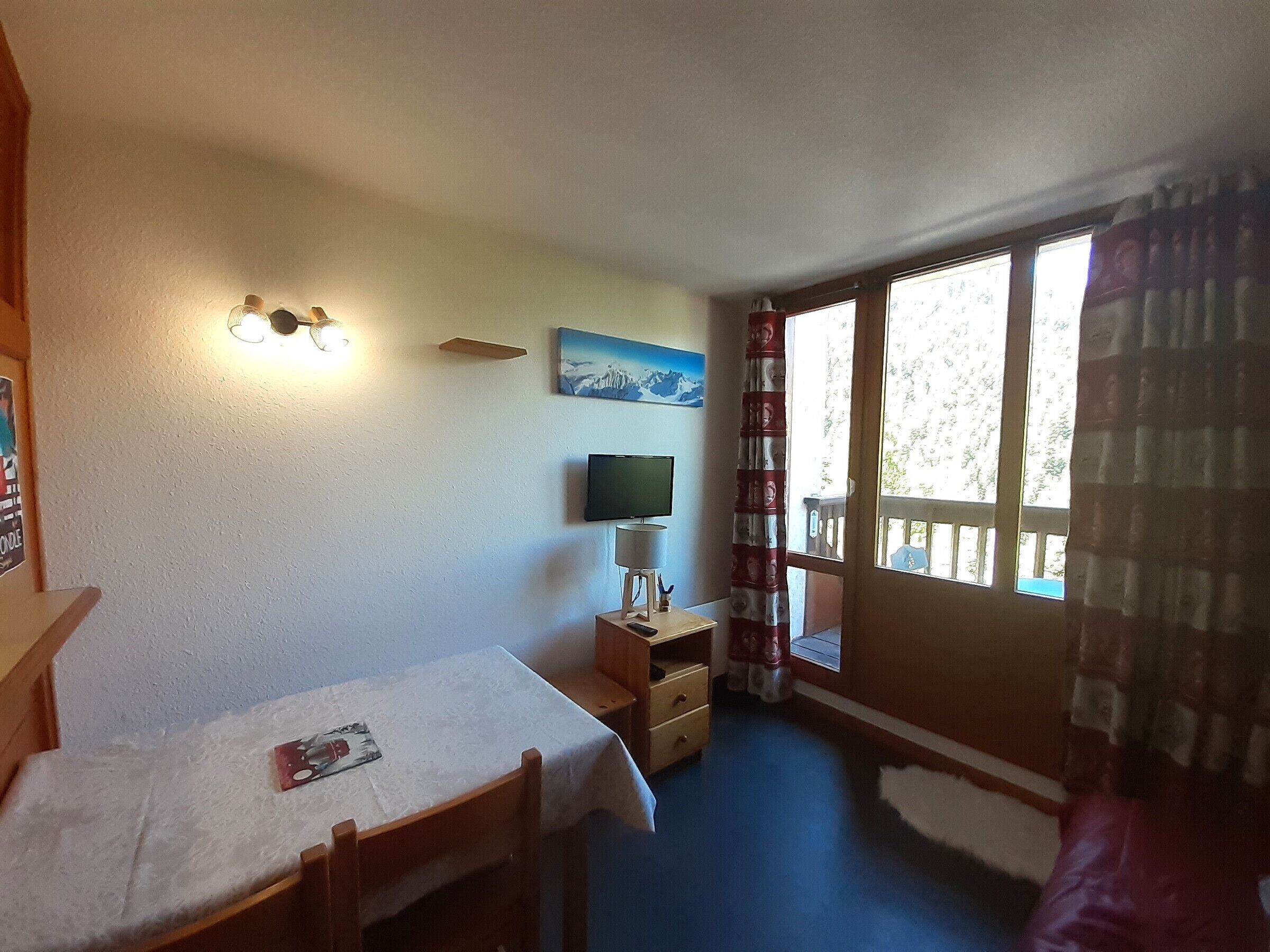 A room with a bed, a desk, a chair, a television, and a window with curtains.