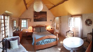 A cozy bedroom with a wooden bed, a round table, and a stone wall. - Normandieheritage14 - Moulin de la Bretonnière - D-Day Tour Guide: E-bike & Hiking (Moulin de la Bretonnière)