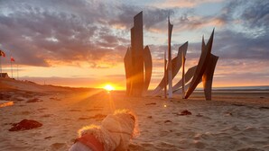 A person lying on the sand with a sunset in the background and abstract sculptures. - Normandieheritage14 - Moulin de la Bretonnière - D-Day Tour Guide: E-bike & Hiking (Moulin de la Bretonnière)