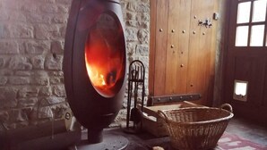 A rustic room with a stone wall, a wooden door, and a large, modern wood-burning stove. - Normandieheritage14 - Moulin de la Bretonnière - D-Day Tour Guide: E-bike & Hiking (Moulin de la Bretonnière)