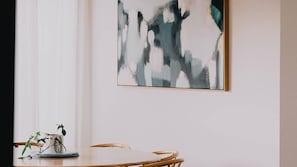 A dining area with a table and chairs, a wall-mounted abstract painting, and a small potted plant on the table. - Berghaus Bright  - Where design meets the mountains - (Bright)