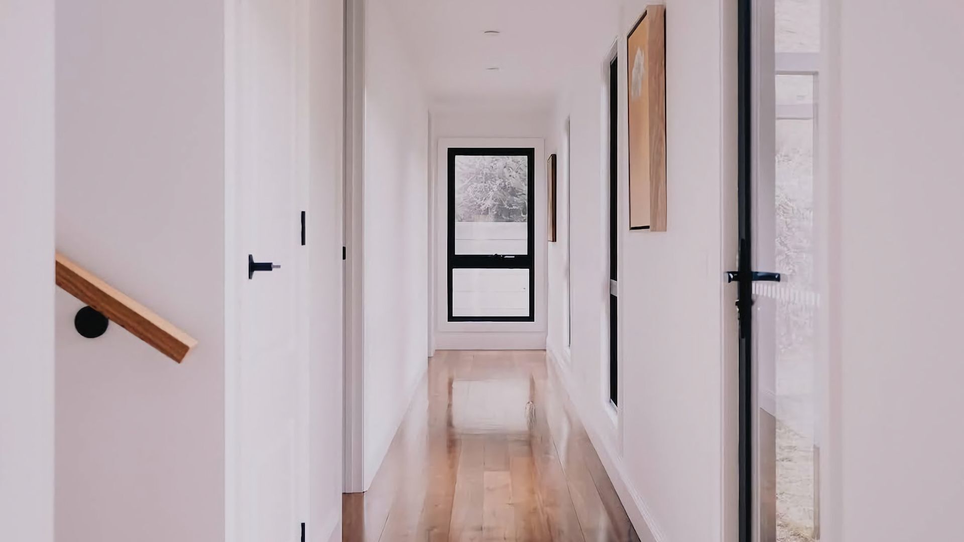 A hallway with a wooden floor, white walls, and a door at the end.