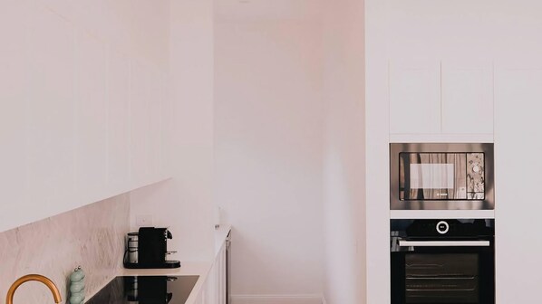 A kitchen with a coffee machine, oven, and a microwave.