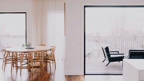 A modern interior with a round dining table and chairs, a large sliding glass door leading to an outdoor deck with a view of a snowy landscape.