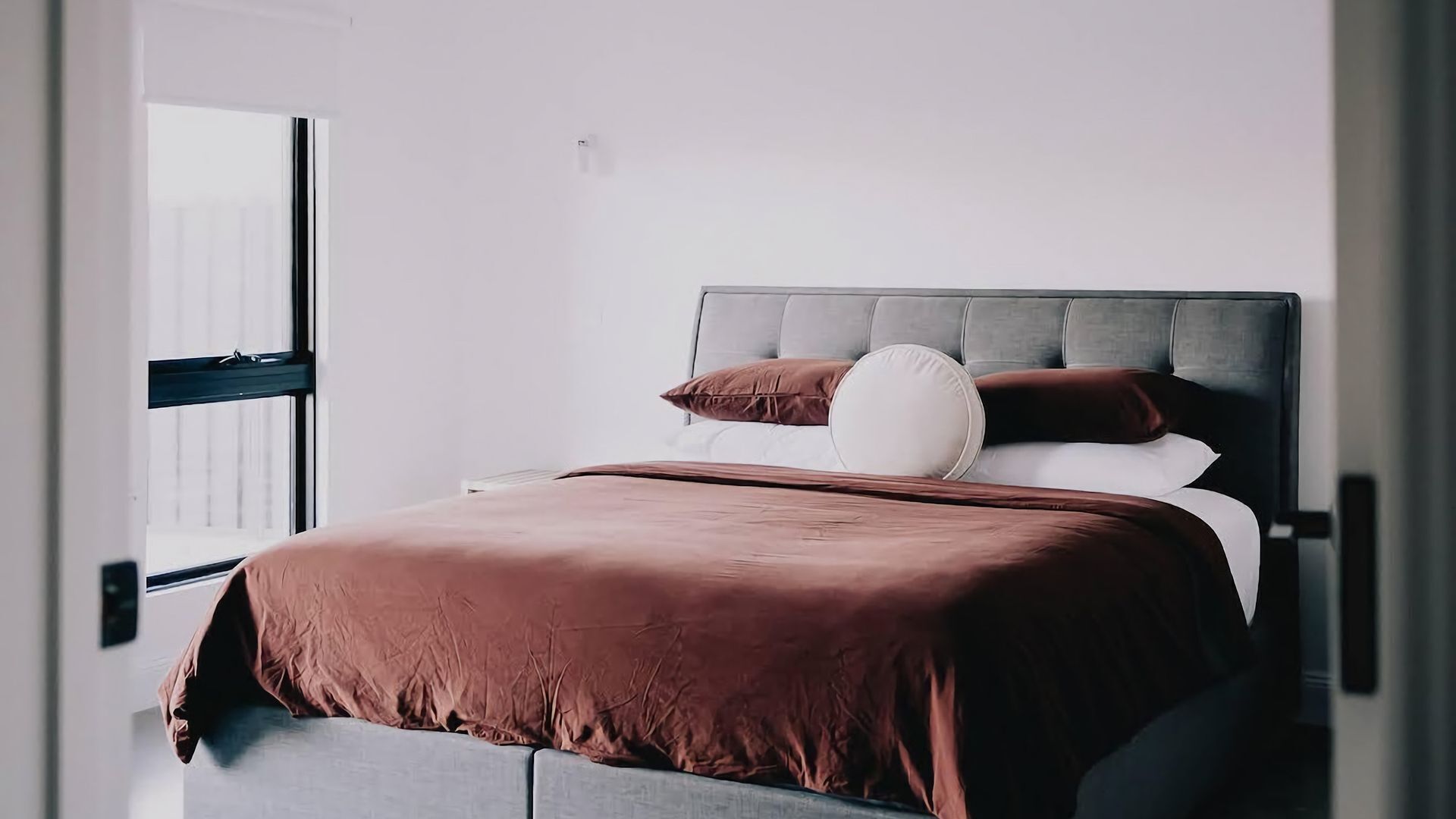 A bed with a grey headboard, brown bedding, and white pillows.