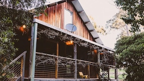 A rustic wooden building with a sloped roof, a satellite dish, and a covered porch with vines. - Way Out Wandi - Country charm in historic Wandiligong (Wandiligong)