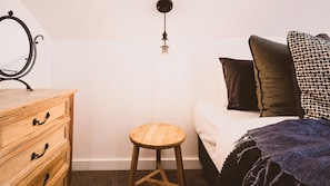 Ein Schlafzimmer mit einem Holzkasten, einem Hocker, einem Bett mit Kissen und einer Pendelleuchte.