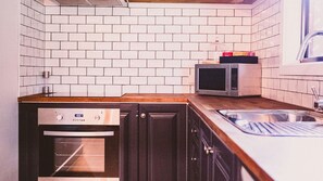 A kitchen with white tiled walls, a microwave, a dishwasher, and wooden cabinets.
