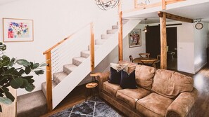 A living room with a staircase, a sofa, a coffee table, and a plant.
