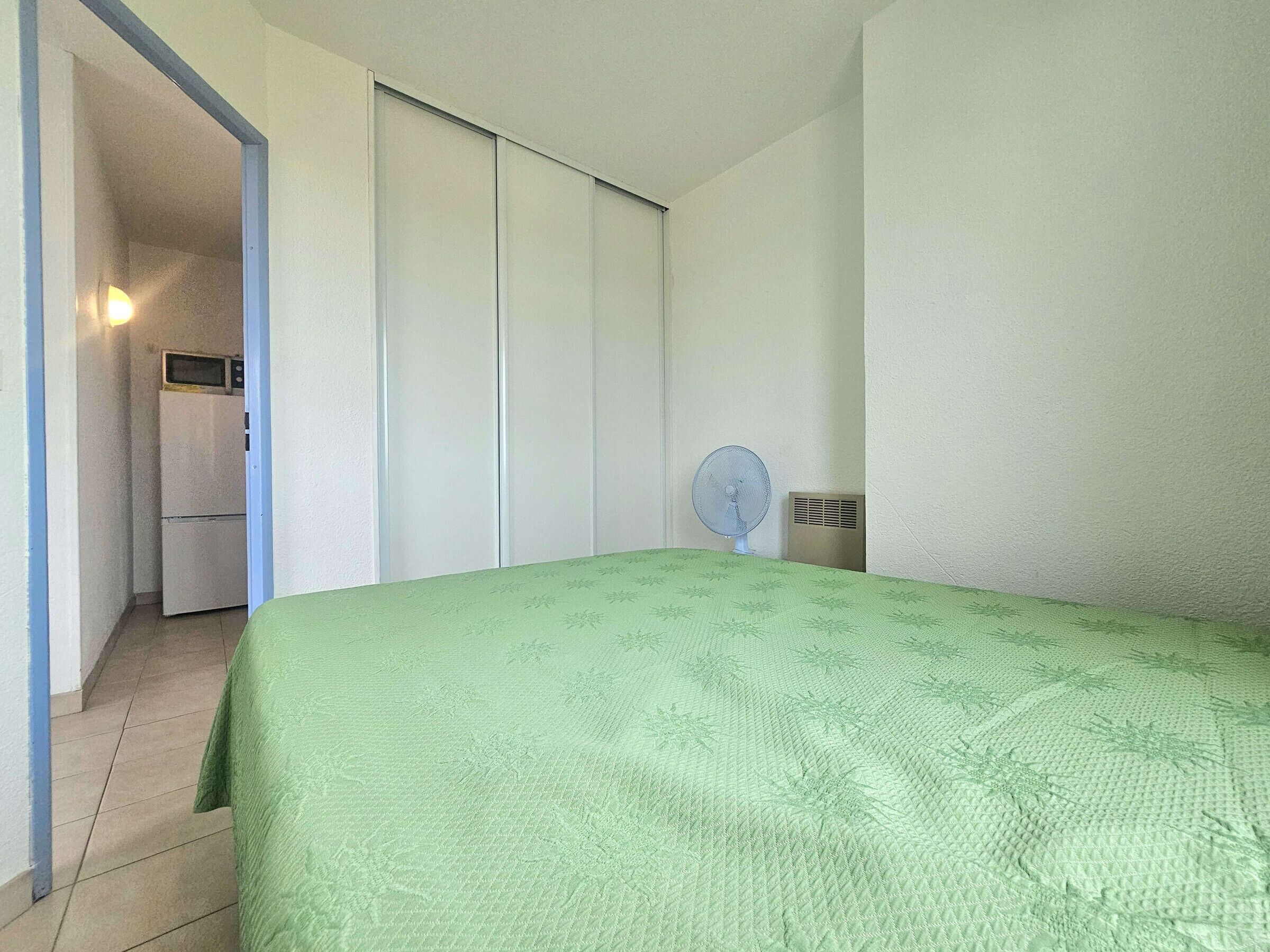 Un dormitorio con una cama, un ventilador, y un microondas junto a un refrigerador.