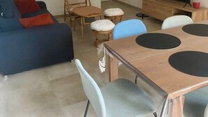 A living room with a blue sofa, a wooden dining table with four chairs, a TV on a stand, and a small plant. - très bel F3 avec balcon (Amélie-les-Bains-Palalda)