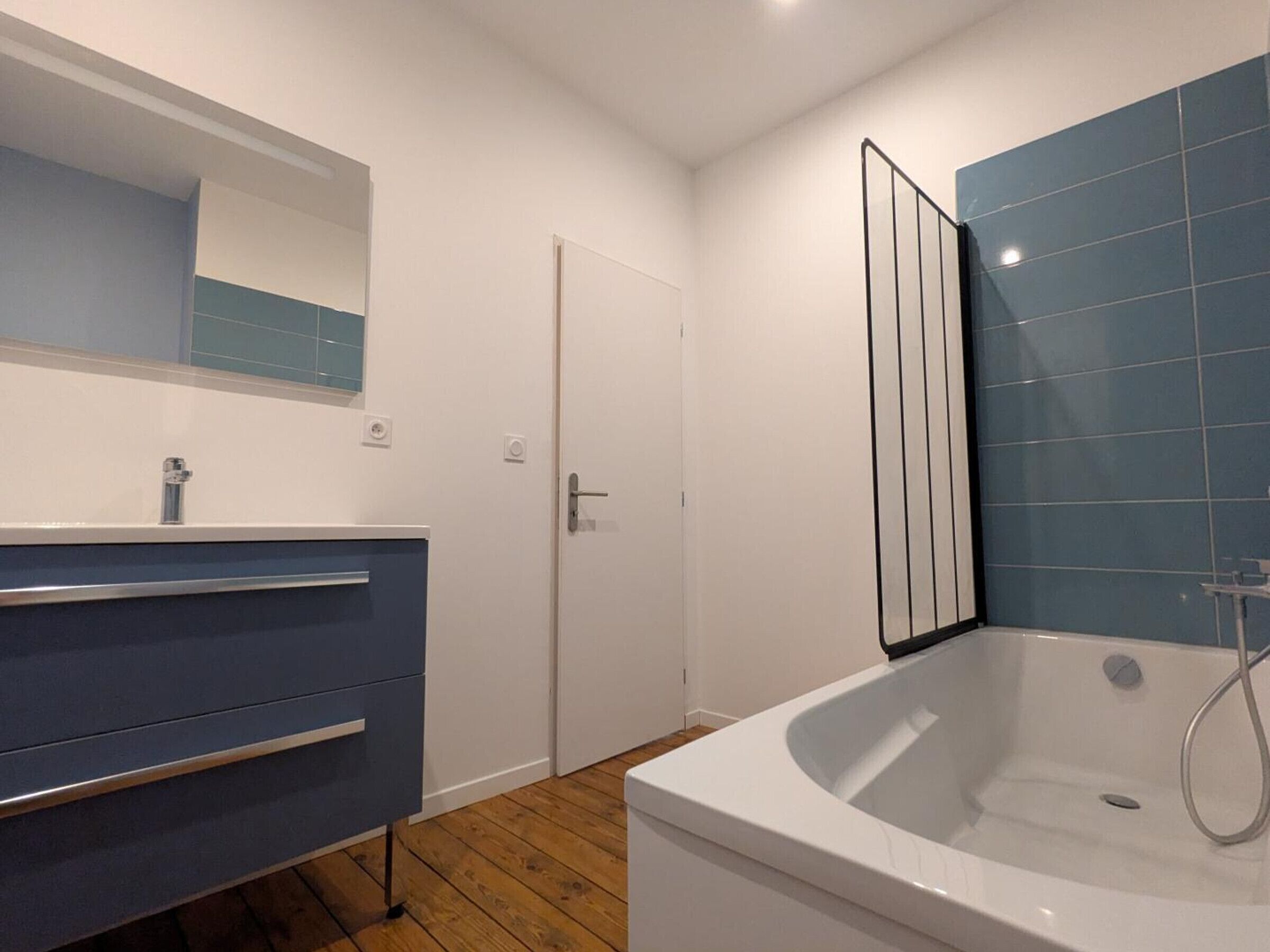 Un baño moderno con una bañera blanca, un tocador azul y un espejo grande.