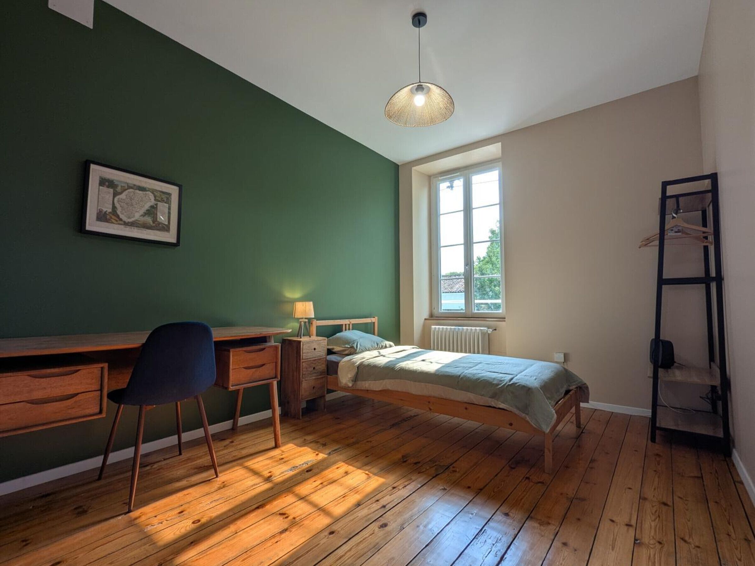 A bedroom with a wooden desk, a bed, a radiator, and a window.